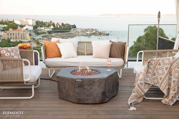 Gaskamin von Elementi in Steinoptik auf einer Holzterrasse mit Outdoormöbeln und hellem Küstenblick.