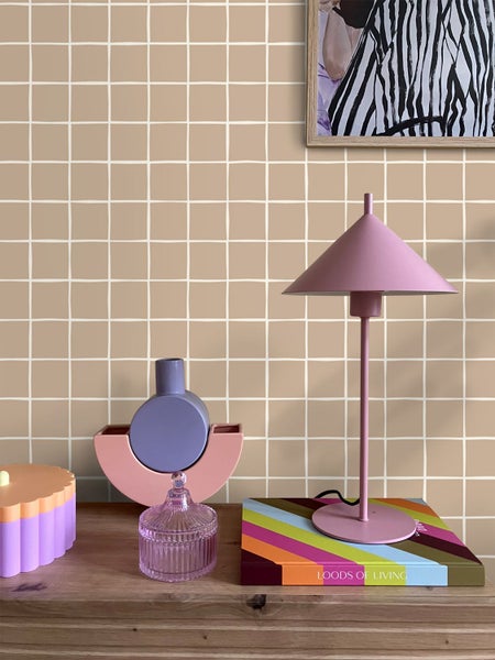 Dekorative Gegenstände auf einem Holzmöbelstück vor einer Wand mit quadratischem Muster, inklusive einer Lampe, einer Dose und Vasen.