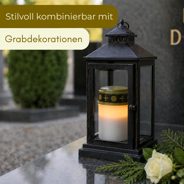 Schwarze Grablaterne aus Metall mit brennender Grabkerze auf einem Grabstein neben einer weißen Rose als Grabdekoration.