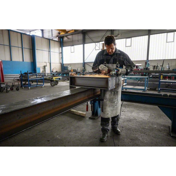 Ein Mann mit Schutzbrille bearbeitet ein Metallstück mit einem Winkelschleifer in einer Werkstatt.