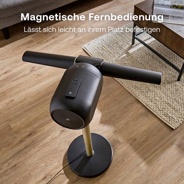 Moderner schwarzer Standventilator mit magnetischer Fernbedienung oben auf dem Gerät, platziert auf Holzboden in einem hellen Wohnzimmer.