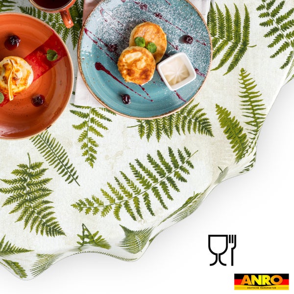 Abwaschbare Tischdecke mit botanischem Farn-Muster, gedeckt mit Tellern und Speisen. Inklusive Symbol lebensmittelecht und ANRO Deutsche Manufaktur Logo.