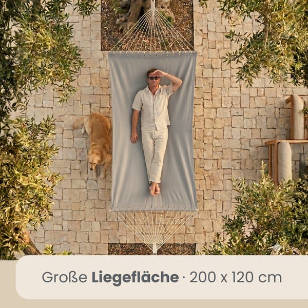 Vogelperspektive einer Hängematte mit 200 mal 120 Zentimeter Liegefläche auf einer Steinterrasse, ein Mann liegt darin und ein Hund liegt daneben.