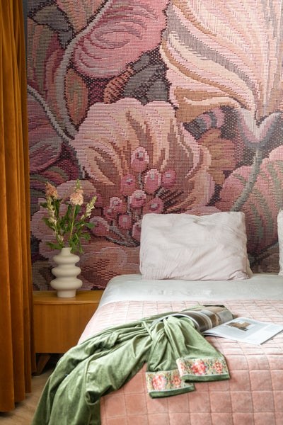 Schlafzimmer mit gemusterter Tapete, Bett, Nachttisch und Blumen