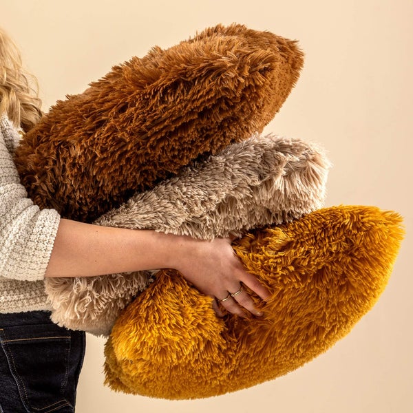 Person hält drei flauschige Langflorkissen in verschiedenen Farben.
