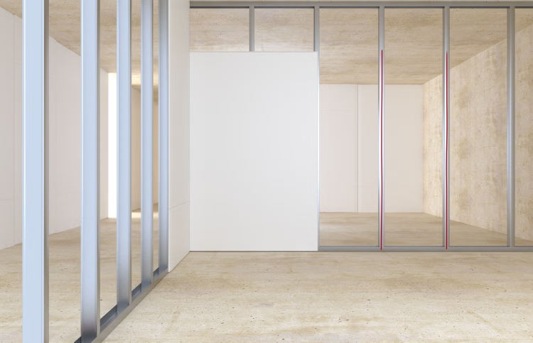 Trockenbauwand im Rohbau mit Metallständerwerk und einer montierten Gipskartonplatte in einem hellen Raum mit Betonboden.