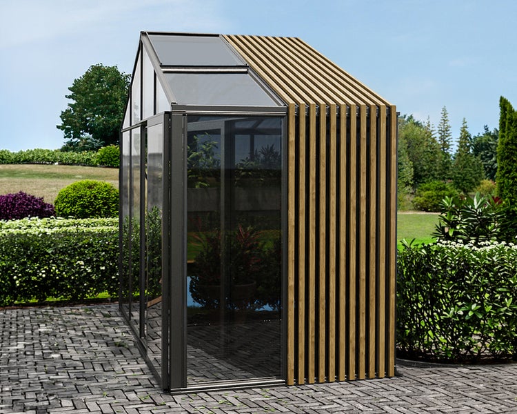 Modernes Gewächshaus mit dunklem Metallrahmen, Glaswänden und Holzlamellen-Fassade auf gepflasterter Terrasse im Garten.