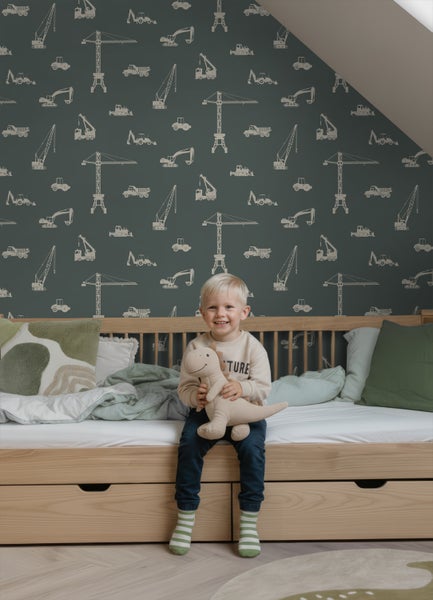 Vliestapete mit Baustellen-Motiv wie Kränen und Baggern im Kinderzimmer an der Wand hinter einem Holzbett.
