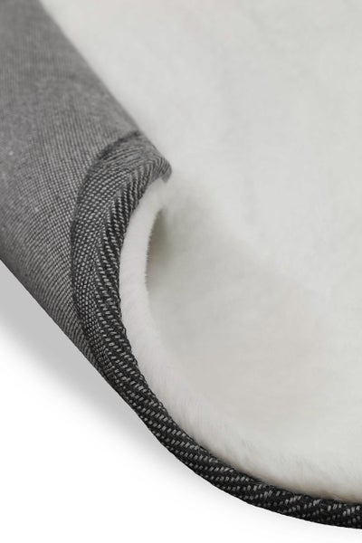 Detailansicht eines weißen, flauschigen Teppichs mit grauer, gewebter Rückseite.