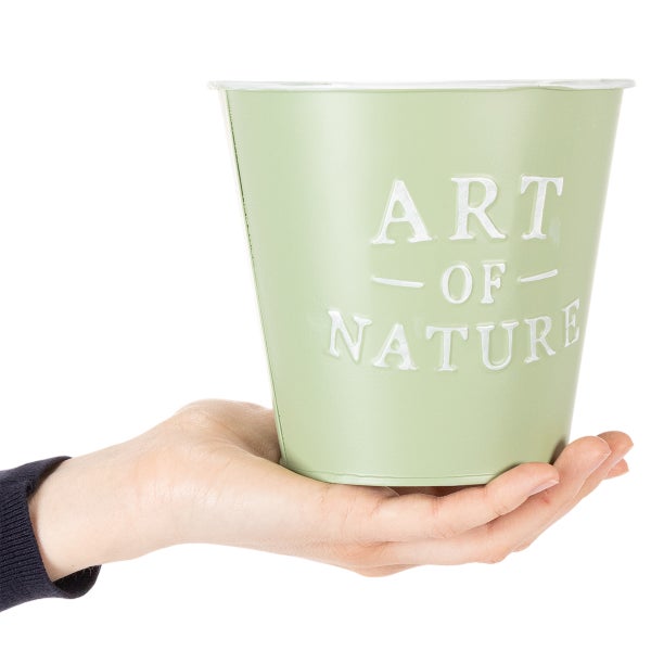 Grüner Metall-Übertopf mit geprägtem Schriftzug Art of Nature in einer Hand gehalten.