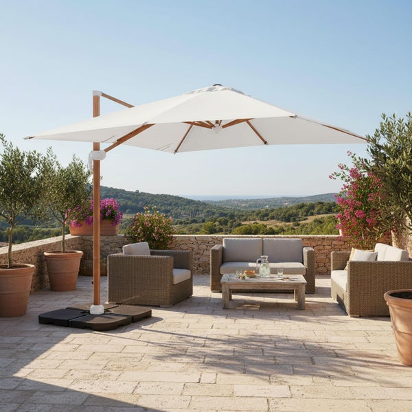 Großer weißer Ampelschirm mit Holzgestell auf einer gepflasterten Terrasse mit Lounge-Möbeln aus Geflecht und Ausblick in die Landschaft.