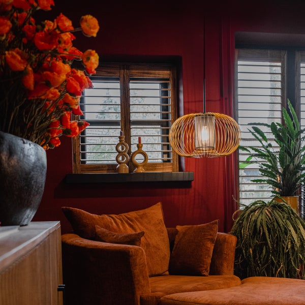 Wohnzimmer mit orangefarbenem Sofa, Hängelampe und Dekoration vor einem Fenster mit Jalousien