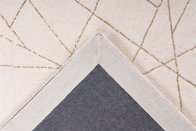 Nahaufnahme eines Teppichs mit geometrischem Muster aus goldenen Linien auf weichem Flor, die strukturierte Textilrückseite an der Ecke zeigend.