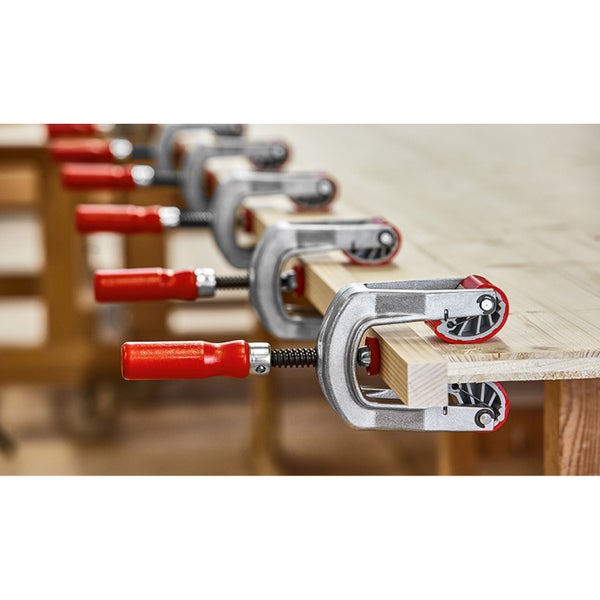 Mehrere Schraubzwingen fixieren Holzstücke auf einer Werkbank.