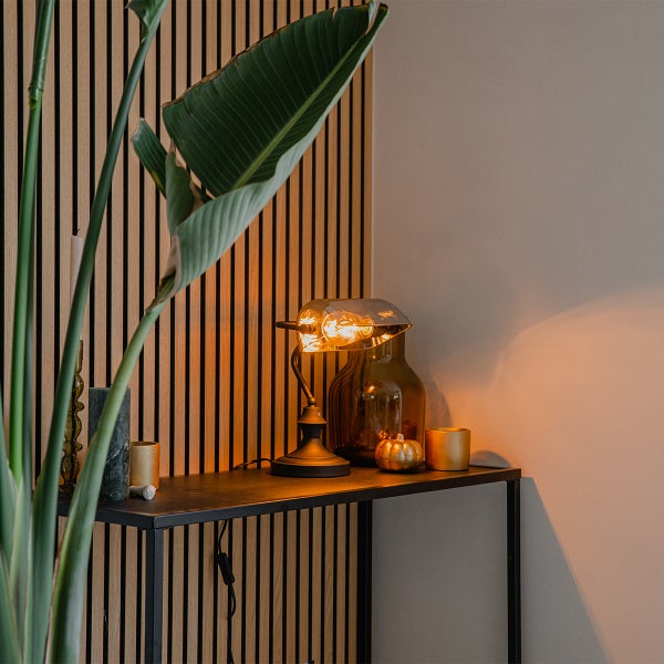 Dekorative Szene mit Stehlampe, Zierkürbis und Pflanze auf einer Konsole vor einer Lamellenwand