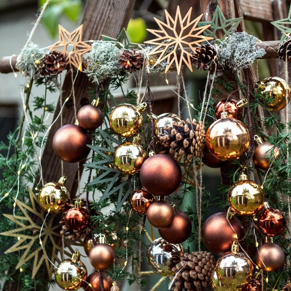 Weihnachtliche Dekoration an einer Holzleiter mit glänzenden und matten Christbaumkugeln, Tannenzapfen, Holzsternen und einer Lichterkette.