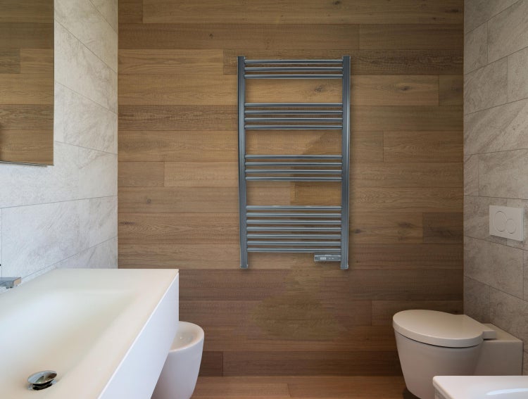 Helles Badezimmer mit Waschtisch, Toilette und Handtuchwärmer an einer Holzwand.