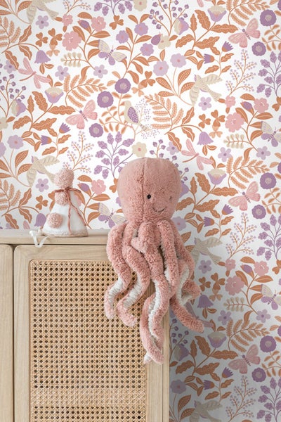 Vliestapete mit floralem Muster, Vögeln und Schmetterlingen in einem Kinderzimmer hinter einem Holzschrank mit Rattanfront und Oktopus-Plüschtier.