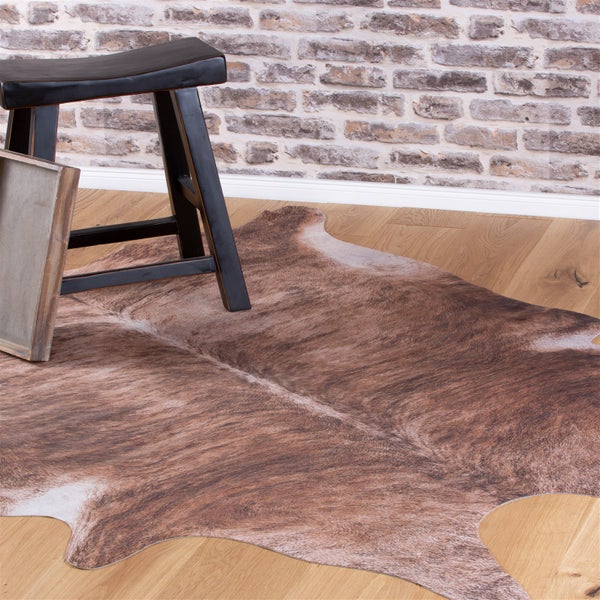 Ein strukturierter Teppich in Kuhfelloptik auf einem Parkettboden mit einem Holzhocker in einem Raum mit Backsteinwand.