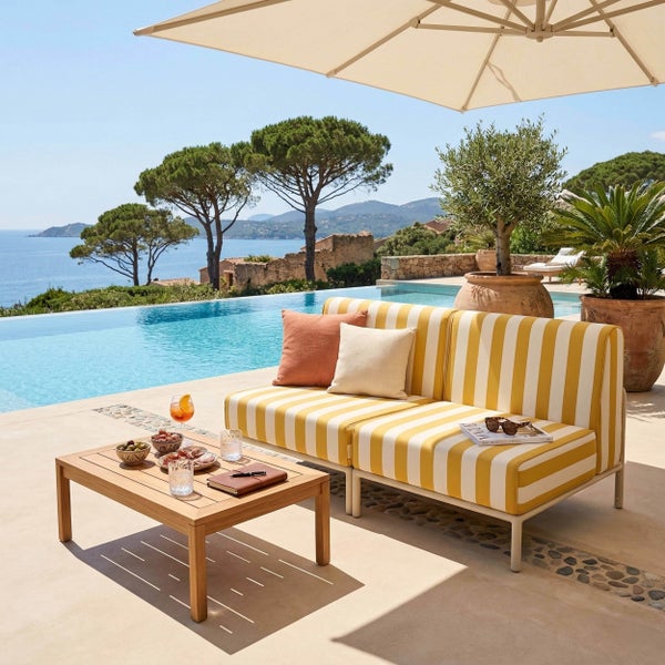 Helle Terrasse mit gelb-weiß gestreiftem Sofa, Holztisch, Infinity-Pool und Sonnenschirm. Mediterraner Stil mit Meerblick.