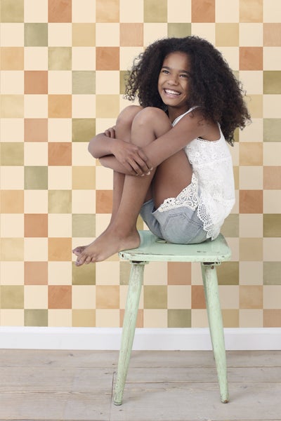 Mädchen sitzt auf einem Hocker vor einer Tapete mit Schachbrettmuster