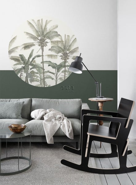 Wohnzimmer mit Sofa, Couchtisch, Stehlampe und Schaukelstuhl vor einer Wand mit Palmenmuster