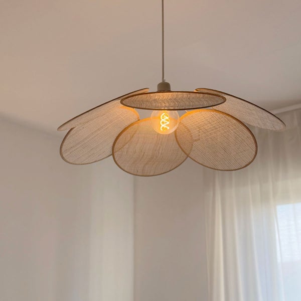 Moderne Hängeleuchte in Blütenform aus geflochtenem Material mit warm leuchtendem Filament Leuchtmittel in einem hellen Wohnraum.