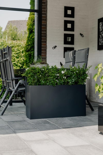 Großer anthrazitfarbener Pflanzkasten mit grünen Pflanzen auf einer modern gestalteten Terrasse mit grauen Bodenfliesen und Gartenmöbeln.