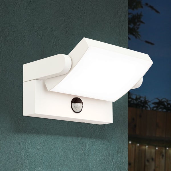 Weiße LED-Außenwandleuchte mit Bewegungsmelder, montiert an einer strukturierten Wand in einer abendlichen Gartenumgebung.