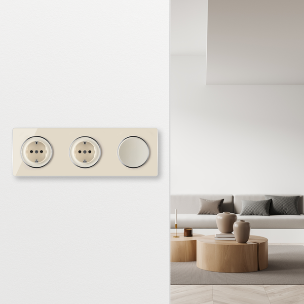 Dreifachrahmen mit zwei Steckdosen und einem Lichtschalter an einer Wand vor einem modern eingerichteten Wohnzimmer