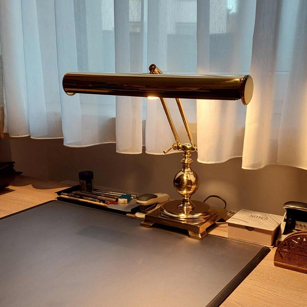 Tischleuchte aus Messing auf einem Schreibtisch vor einem Fenster mit Vorhängen