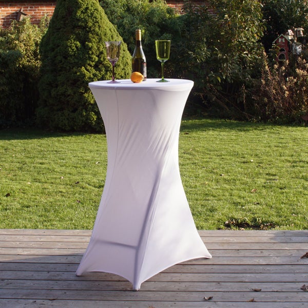 Ein Stehtisch mit einer passenden weißen Stretchhusse steht auf einer Holzterrasse im Garten, dekoriert mit einer Flasche und zwei Weingläsern.