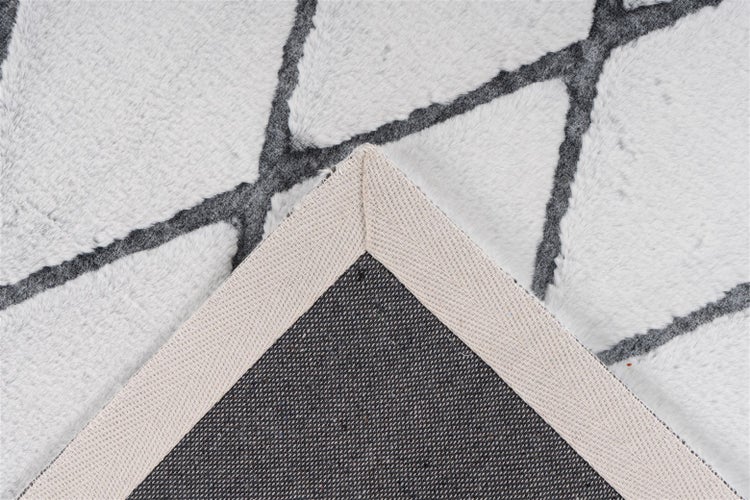 Weicher Teppich mit geometrischem Muster, Detailansicht der umgeschlagenen Ecke und der gewebten Rückseite.