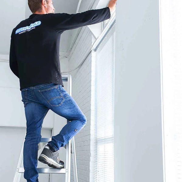 Eine Person steht auf einer Leiter und montiert eine Jalousie.