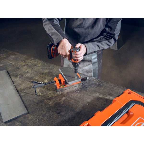 Mann bohrt mit Akkubohrmaschine in Metall, das mit Schraubstock fixiert ist