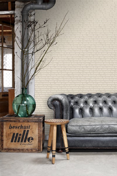 Wohnzimmer mit Sofa, Hocker, Holzkiste und Dekoration vor einer Tapete mit Sportmotiven