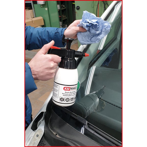 Eine Person reinigt eine Windschutzscheibe mit einem Druckzerstäuber von KS Tools und einem Tuch.