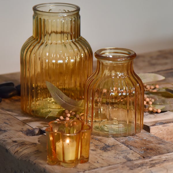 Gerippte Glasvasen in zwei Größen und ein Glaswindlicht mit Teelicht auf einem Holztisch mit dekorativen Zweigen und Beeren.