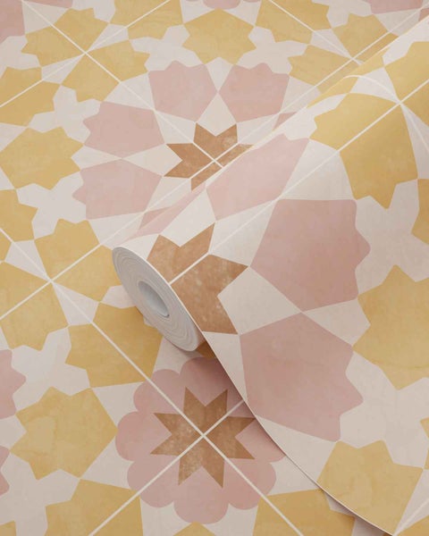 Vliestapete mit geometrischem Fliesenmuster aus Sternen in Gelb und Rosa, eine Rolle liegt auf einer ausgebreiteten Bahn.