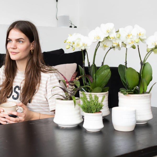 Frau mit Tasse neben Zimmerpflanzen und Kerze auf einem Tisch