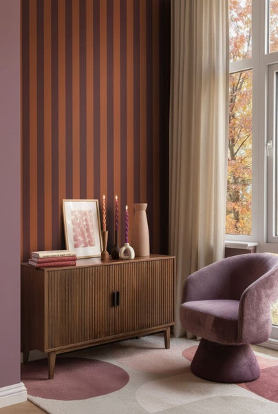 Helles Zimmer mit gestreifter Tapete, Sideboard aus Holz mit Rillenfront und lila Sessel auf gemustertem Teppich.