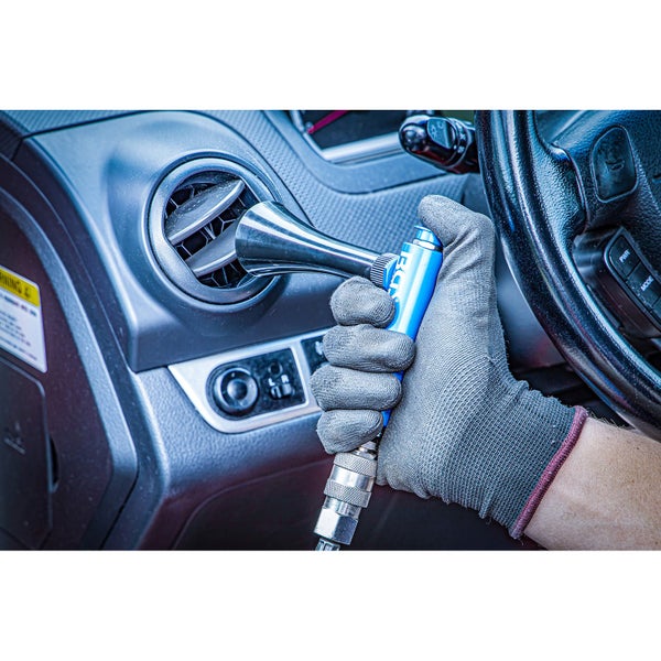 Eine Person reinigt mit einer Druckluftpistole eine Lüftungsöffnung im Auto.