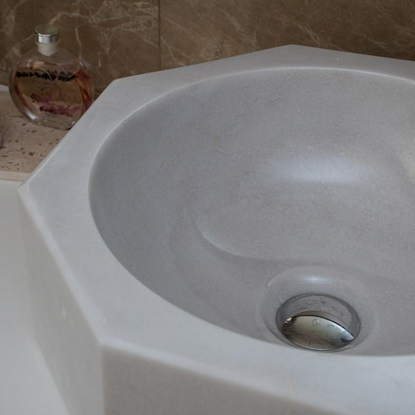 Sechseckiges Aufsatzwaschbecken aus Stein mit rundem Innenbecken und Ablauf im Badezimmer.