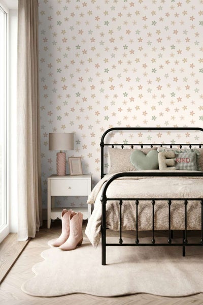 Ein Kinderzimmer mit Vliestapete mit Blumenmuster, einem schwarzen Metallbett und einem Nachttisch mit Lampe.