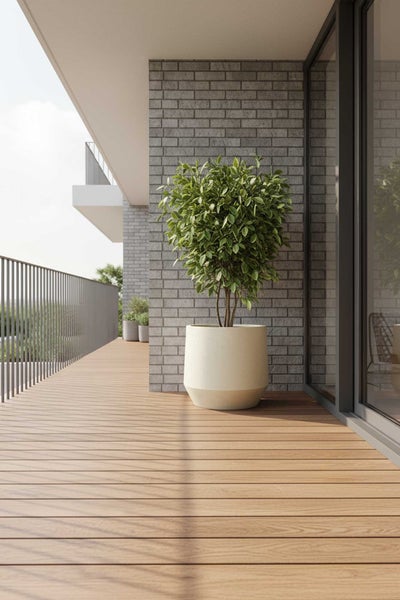 Moderne, helle Balkonszene mit großer grüner Pflanze in beigem konischem Topf, Holzterrasse, grauer Ziegelwand und Metallgeländer.