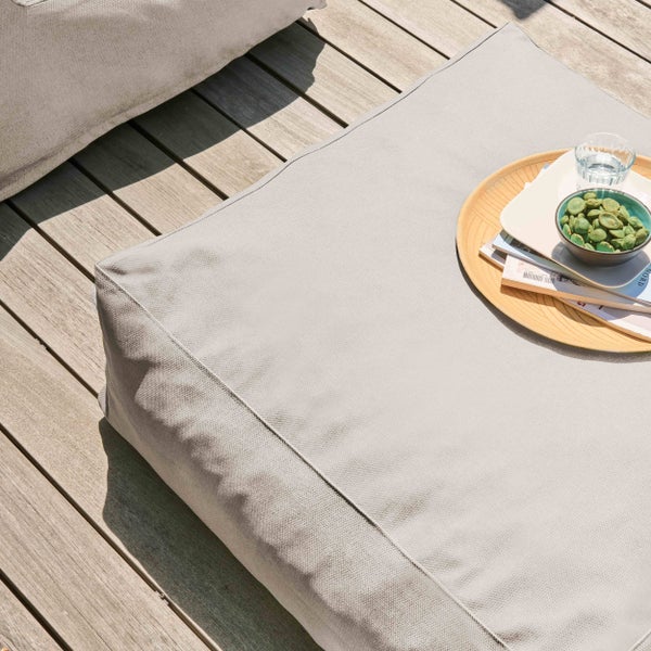 Quadratischer grauer Outdoor-Sitzsack auf einer Holzterrasse mit einem Tablett und Snacks darauf.