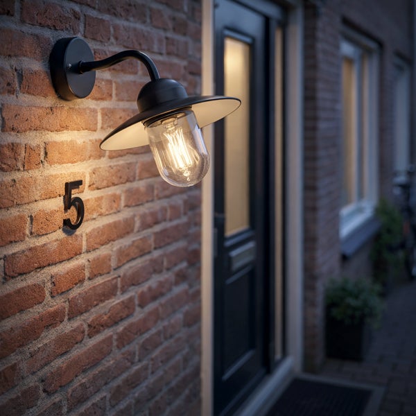 Schwarze Außenwandleuchte mit klarem Glas und Filament-Leuchtmittel an einer Ziegelwand mit Hausnummer fünf neben einer Tür.