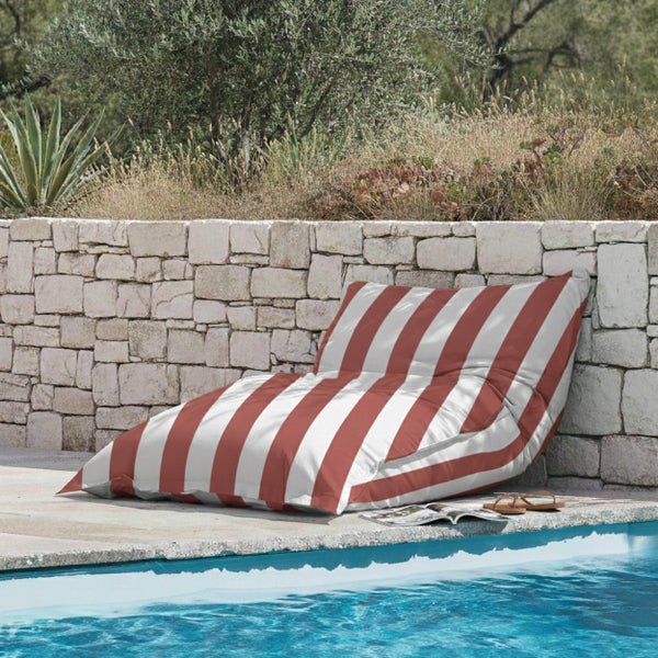 Gestreifter Sitzsack im Außenbereich an einem Pool vor einer Natursteinmauer.