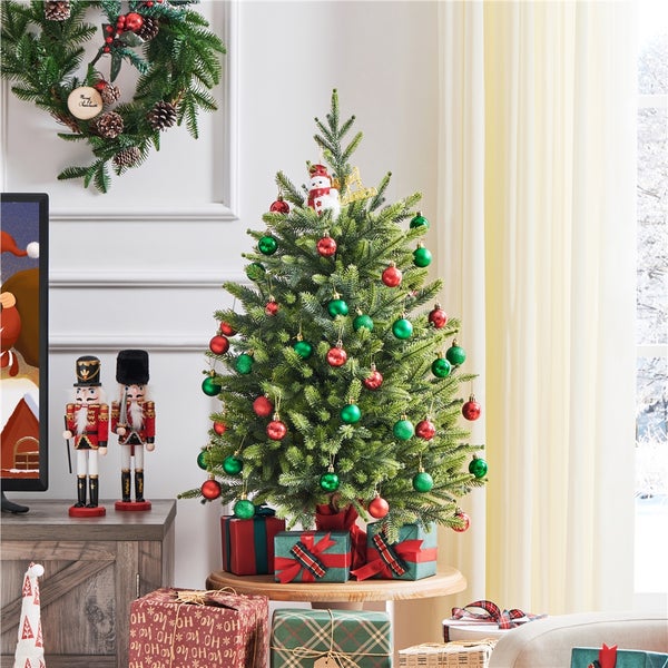 Weihnachtliche Wohnzimmerszene mit kleinem Weihnachtsbaum, geschmückt mit roten und grünen Kugeln, Geschenken und Dekorationen.