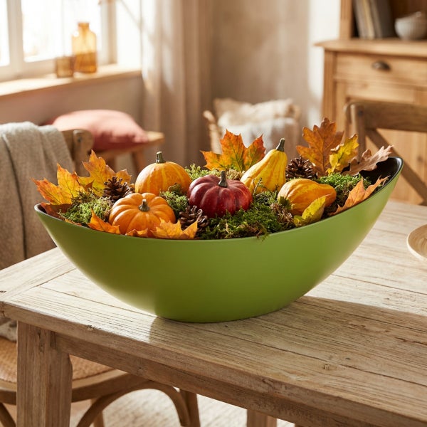 Herbstliche Tischdekoration mit Kürbissen, Ahornblättern und Moos in einer länglichen Schale aus Kunststoff auf einem Holztisch.